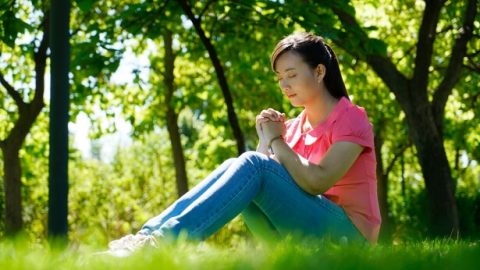 一个年轻姊妹坐在草地上祷告